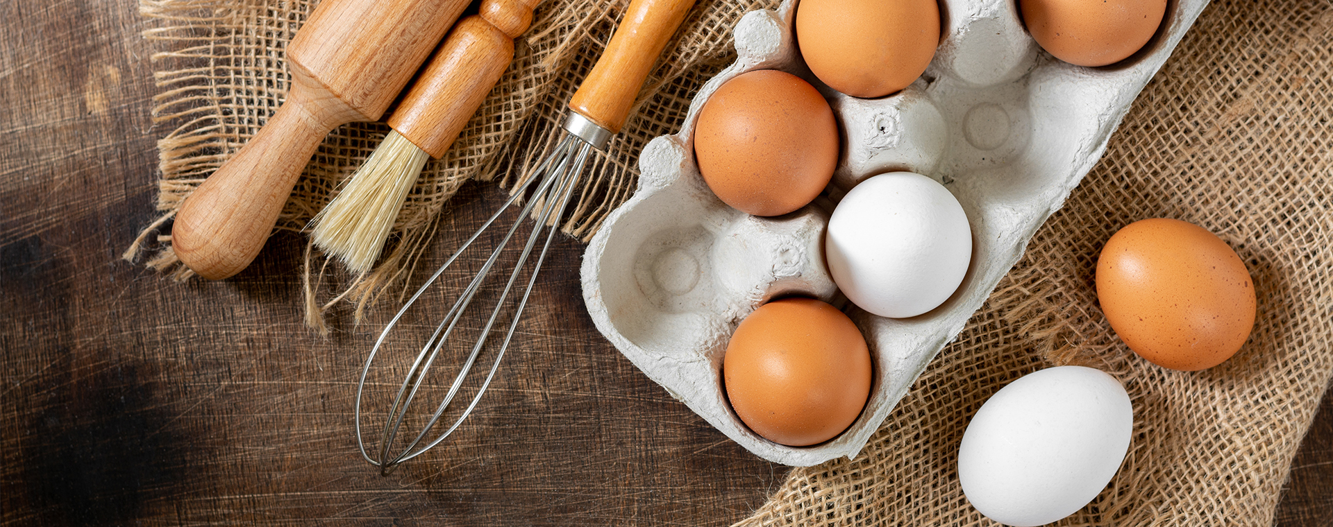 close up of brown and white eggs in a carton next to kitchen utensils