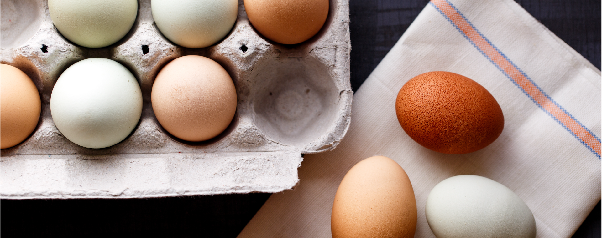 Egg carton with mix of white and brown eggs on a table next to three eggs