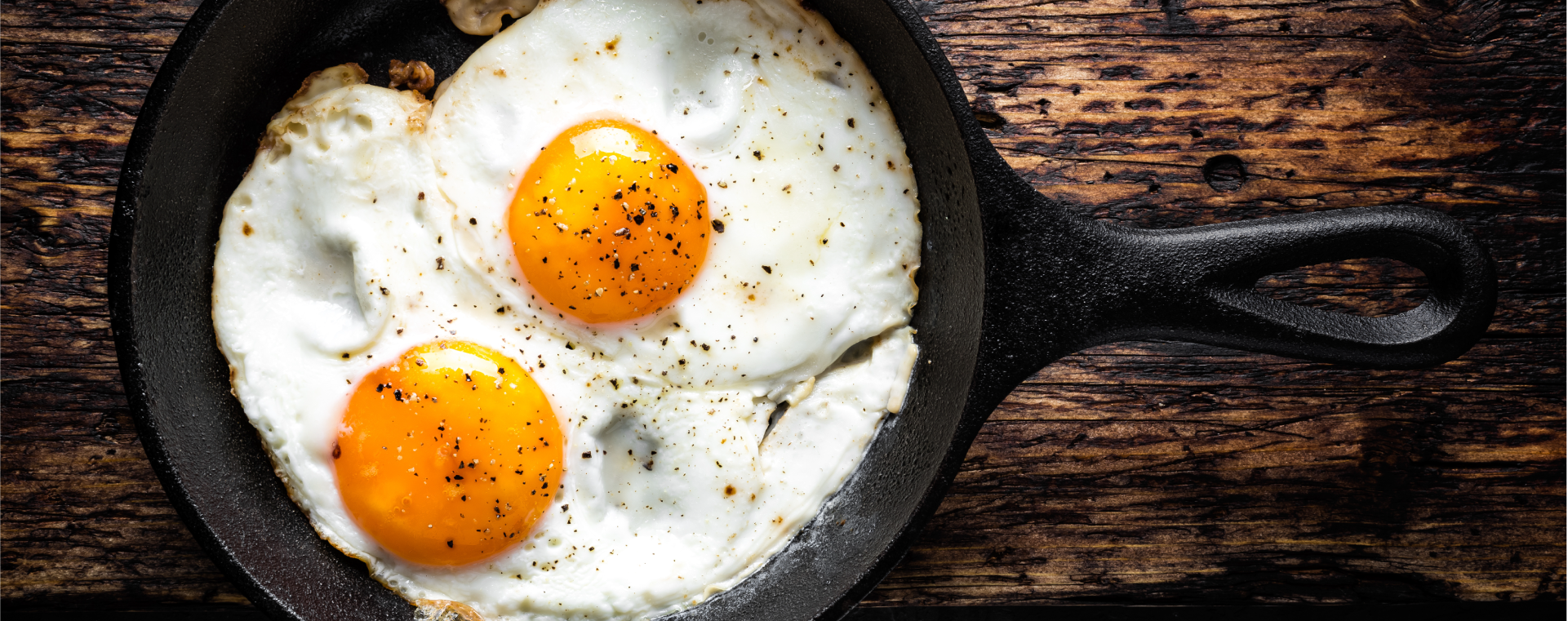 Two sunny-side eggs in a cast iron pan with black pepper sprinkled on top