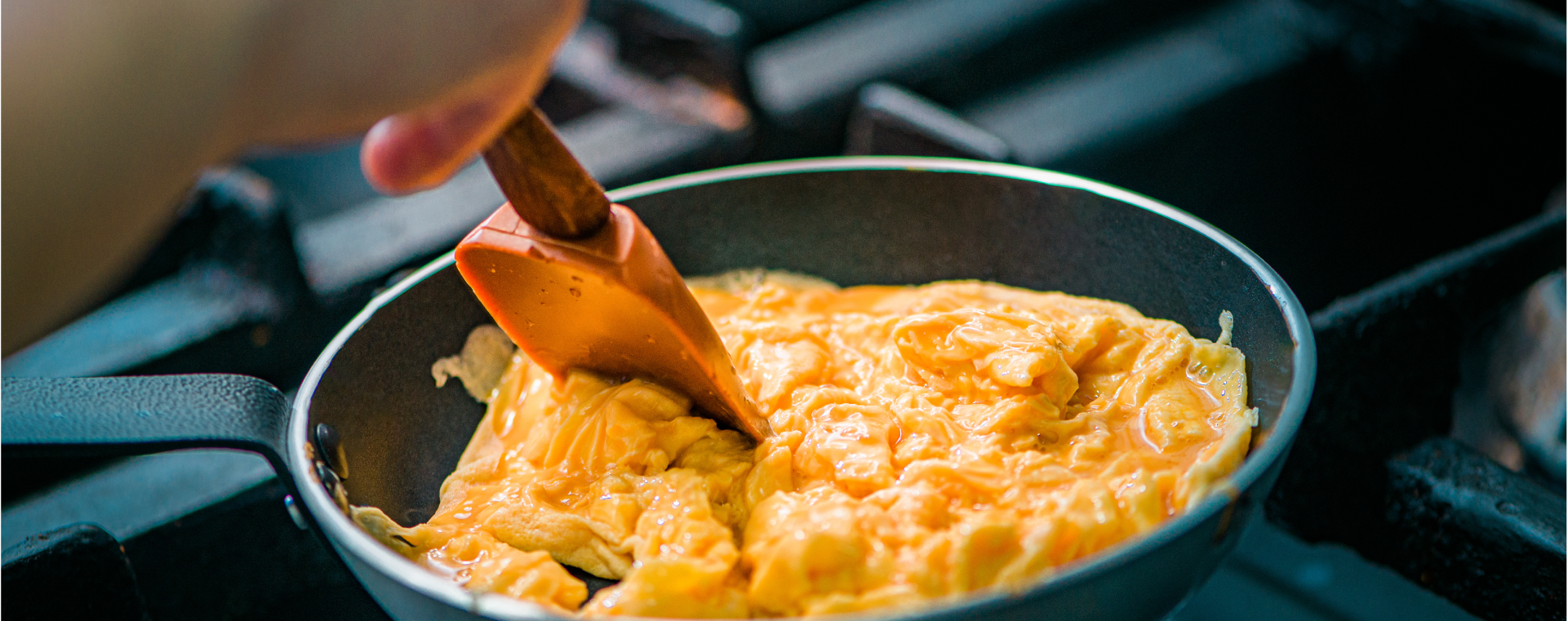 Scrambled eggs in a pan being stirred by a plastic spatula