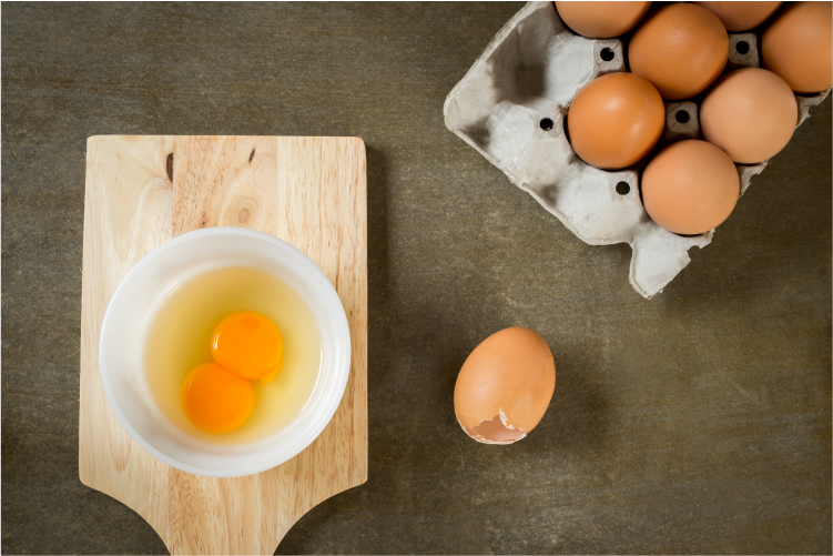 An egg that is cracked open showing two yolks in one bowl