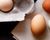 Three pasture-raised eggs on a piece of linen next to an egg carton of eggs