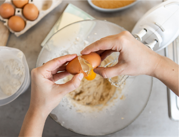 Cracking an egg over a glass bowl half-full with wet batter