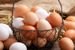 Wire basket filled with brown and white eggs surrounded by more eggs on a wooden table