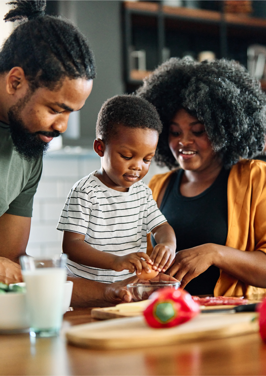 Dad and mom showing toddler how to crack egg in a kitchen