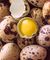 A quail egg broken in half with the yolk intact, laying on a pile of quail eggs